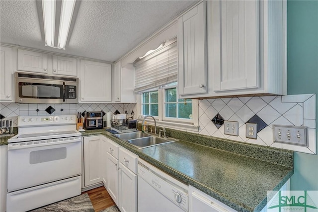 kitchen featuring white appliances, dark countertops, a sink, and white cabinetry