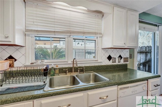 kitchen featuring dark countertops, a healthy amount of sunlight, white cabinets, white dishwasher, and a sink