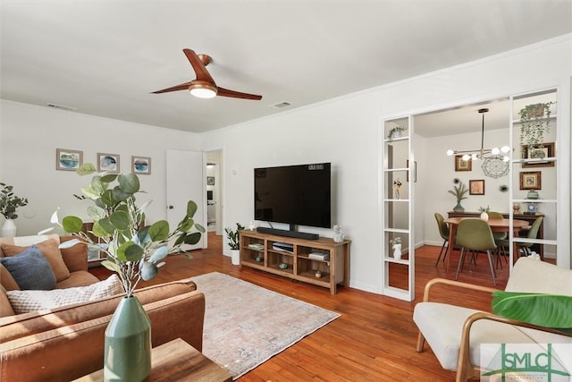 living room with ceiling fan with notable chandelier, visible vents, crown molding, and wood finished floors