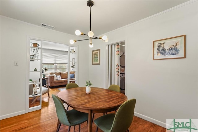 dining room with light wood finished floors, stacked washer / dryer, visible vents, and crown molding