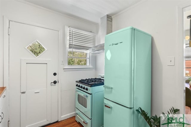 kitchen with range with gas stovetop, freestanding refrigerator, crown molding, and wall chimney range hood