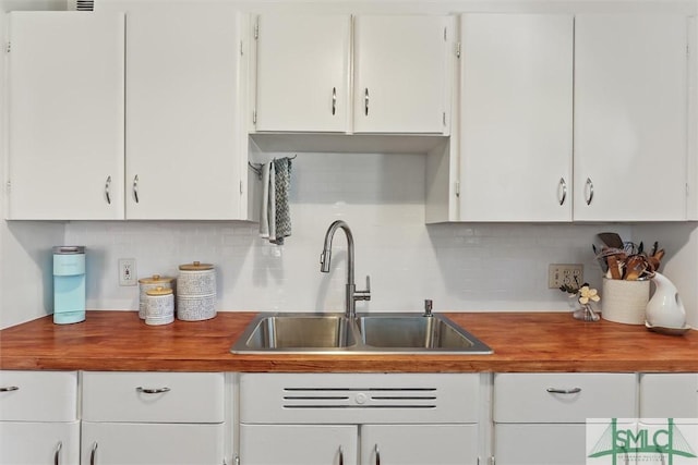 kitchen with butcher block countertops, white cabinets, and a sink