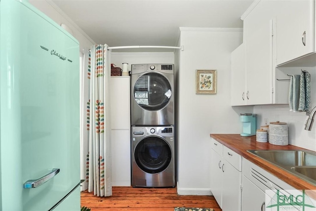 clothes washing area featuring laundry area, light wood finished floors, stacked washer / dryer, crown molding, and a sink