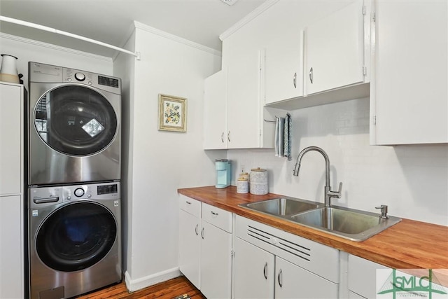 washroom with cabinet space, ornamental molding, a sink, stacked washing maching and dryer, and baseboards