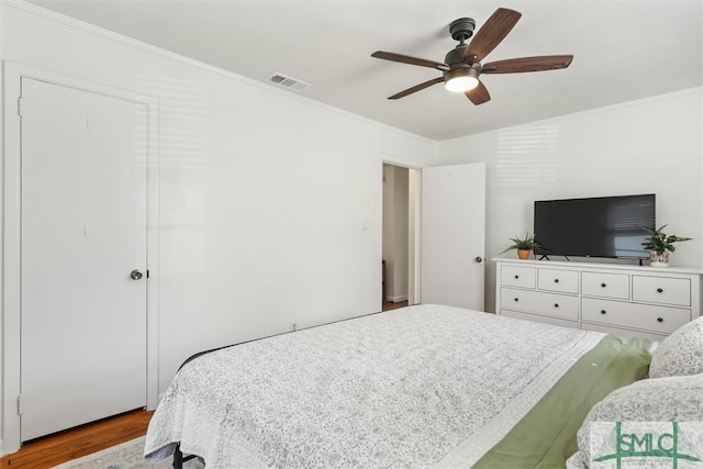 bedroom with a ceiling fan, wood finished floors, visible vents, and crown molding