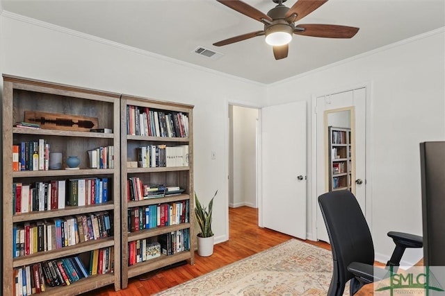 home office with crown molding, visible vents, a ceiling fan, wood finished floors, and baseboards