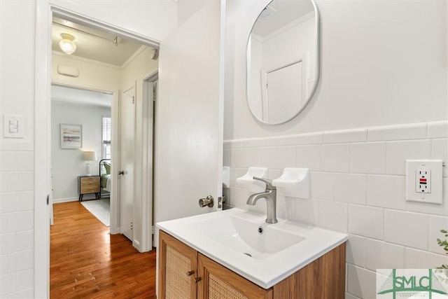 bathroom with wainscoting, ornamental molding, wood finished floors, vanity, and tile walls