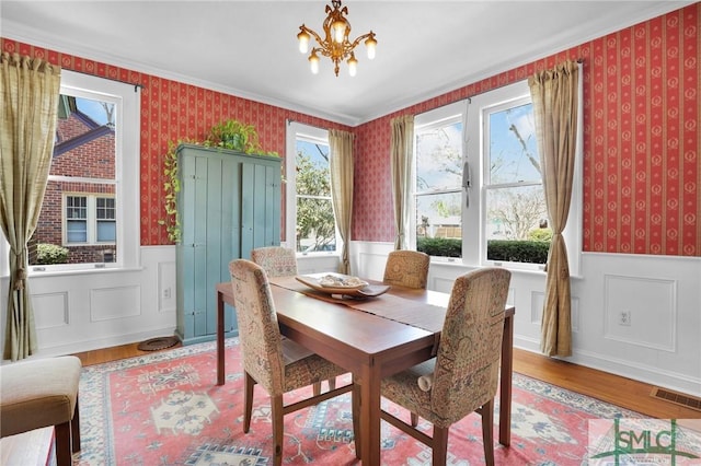 dining area with wallpapered walls, visible vents, wood finished floors, and wainscoting