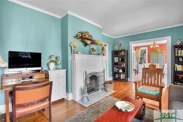 living area with baseboards, a fireplace with flush hearth, ornamental molding, wood finished floors, and a notable chandelier