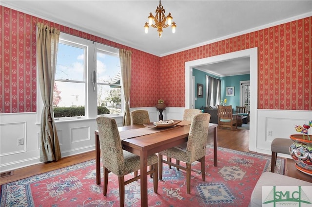 dining room with a chandelier, wood finished floors, a wainscoted wall, and wallpapered walls