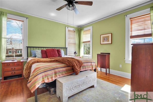 bedroom with multiple windows, crown molding, baseboards, and wood finished floors