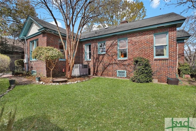 rear view of house with cooling unit, brick siding, a yard, and a chimney