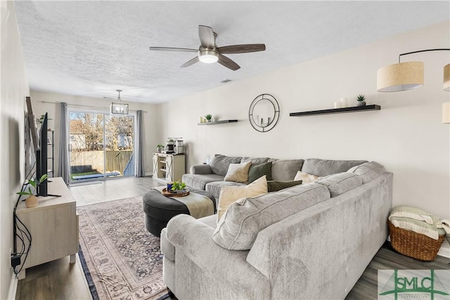 living room featuring dark wood finished floors, visible vents, a textured ceiling, and a ceiling fan