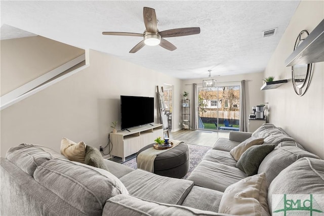 living room with a textured ceiling, a ceiling fan, visible vents, and light wood-type flooring