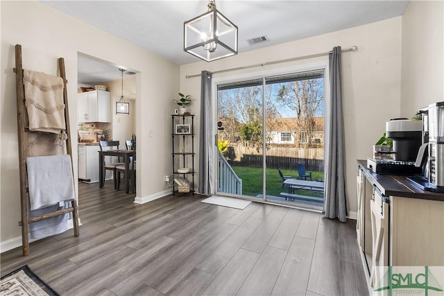 dining area with baseboards, wood finished floors, visible vents, and a chandelier