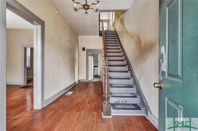 stairs with a notable chandelier, wood finished floors, and baseboards