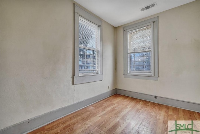 unfurnished room with light wood finished floors, visible vents, and baseboards