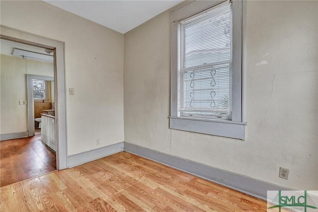 empty room featuring light wood finished floors, attic access, and baseboards