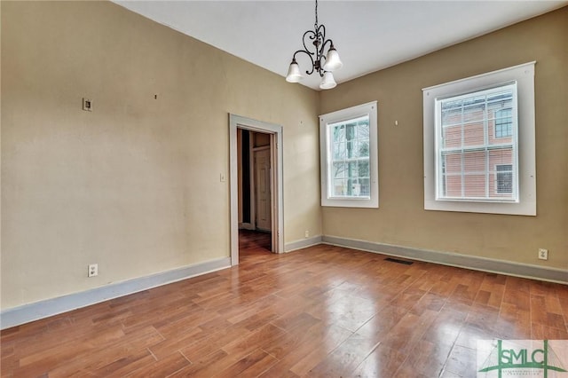 empty room featuring visible vents, a notable chandelier, baseboards, and wood finished floors