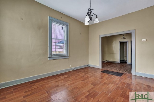 unfurnished room with a chandelier, baseboards, and wood finished floors