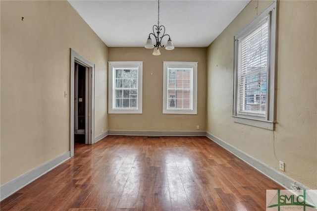 unfurnished dining area featuring a notable chandelier, wood-type flooring, and baseboards