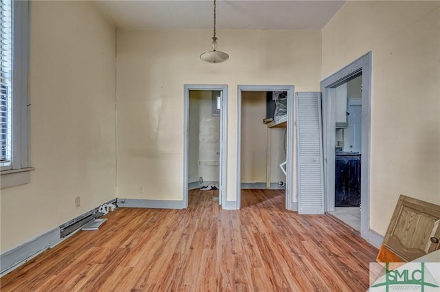 unfurnished bedroom featuring ensuite bath, light wood-type flooring, a walk in closet, and baseboards