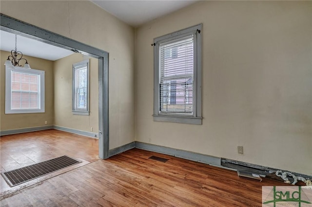 spare room with baseboards, wood finished floors, visible vents, and a notable chandelier