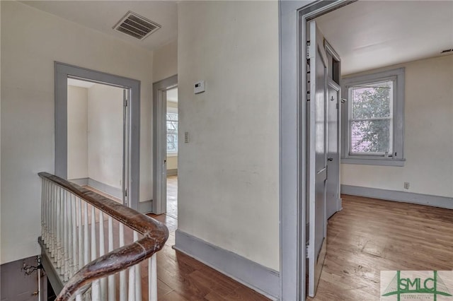 hallway with a wealth of natural light, wood finished floors, visible vents, and baseboards