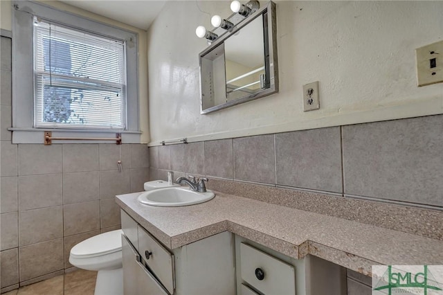 bathroom with toilet, vanity, tile walls, wainscoting, and tile patterned floors