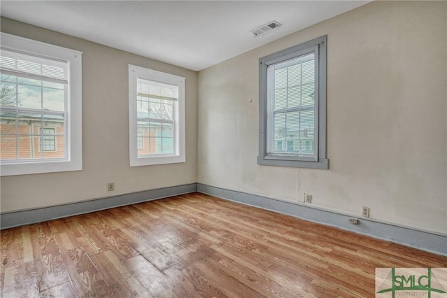 empty room featuring wood finished floors, visible vents, and baseboards