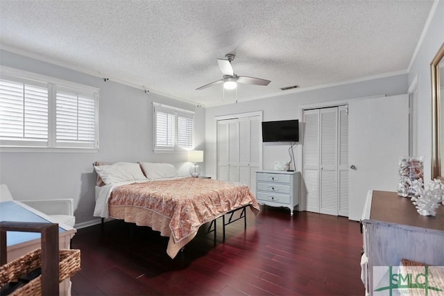 bedroom with ceiling fan, wood finished floors, visible vents, multiple closets, and ornamental molding