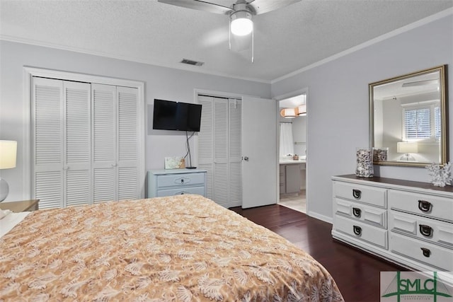 bedroom featuring dark wood-style floors, crown molding, multiple closets, visible vents, and a textured ceiling