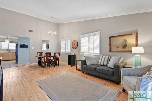 living area with light wood finished floors, baseboards, visible vents, ornamental molding, and a chandelier