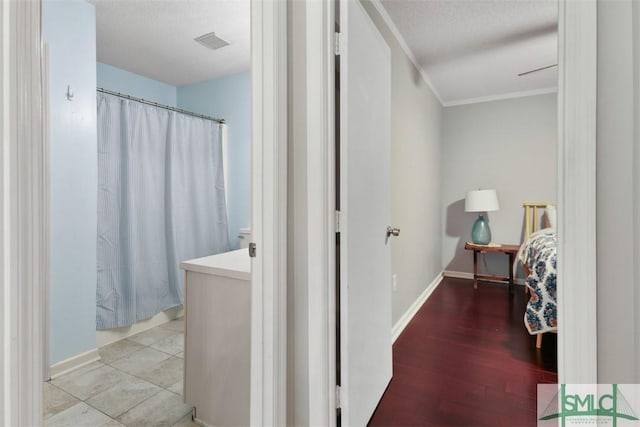 hallway with a textured ceiling, light wood-type flooring, visible vents, and baseboards