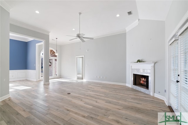 unfurnished living room with light wood finished floors, a tile fireplace, a ceiling fan, and crown molding