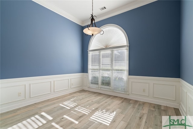 spare room featuring light wood-style floors, wainscoting, visible vents, and ornamental molding