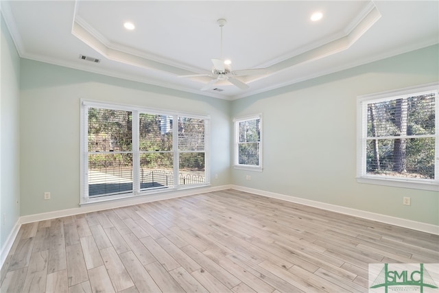 empty room featuring light wood finished floors, visible vents, a tray ceiling, and crown molding