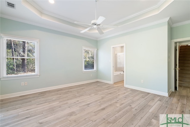 unfurnished bedroom with a tray ceiling, visible vents, light wood-style floors, ornamental molding, and baseboards