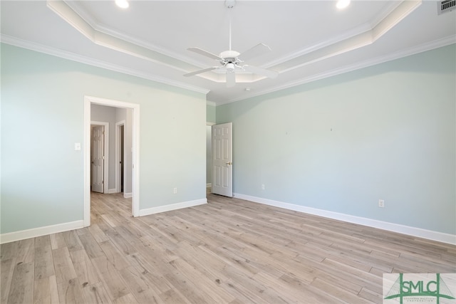 spare room with a tray ceiling, baseboards, crown molding, and light wood finished floors