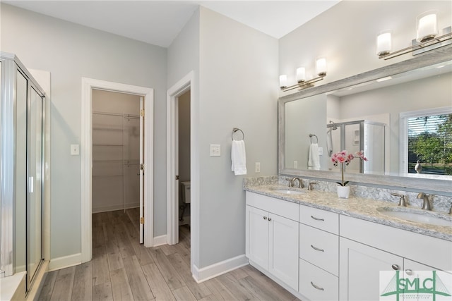 bathroom featuring double vanity, a sink, a shower stall, and wood finished floors