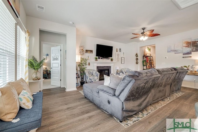 living room with a glass covered fireplace, a wealth of natural light, wood finished floors, and visible vents