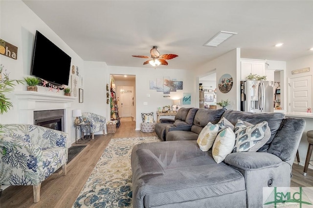 living room featuring light wood finished floors, ceiling fan, and a glass covered fireplace