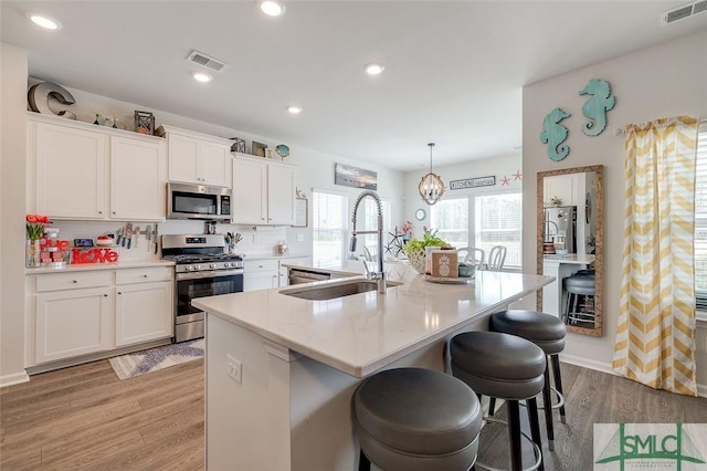 kitchen with visible vents, light wood-style flooring, appliances with stainless steel finishes, a sink, and an island with sink