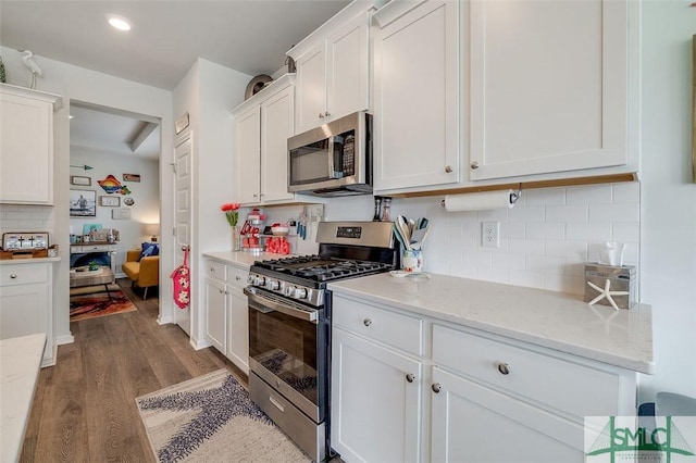 kitchen featuring light stone counters, stainless steel appliances, wood finished floors, white cabinetry, and backsplash