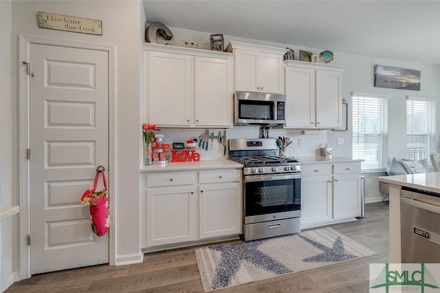 kitchen featuring white cabinets, light countertops, appliances with stainless steel finishes, light wood finished floors, and tasteful backsplash