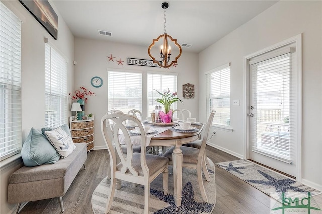 dining room with baseboards, wood finished floors, visible vents, and an inviting chandelier