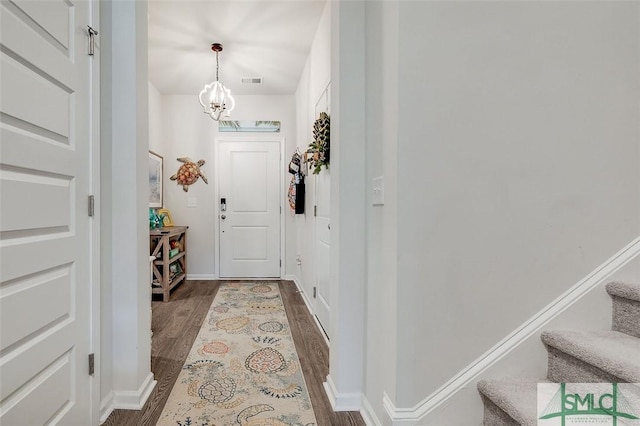 doorway to outside with a notable chandelier, wood finished floors, visible vents, baseboards, and stairs