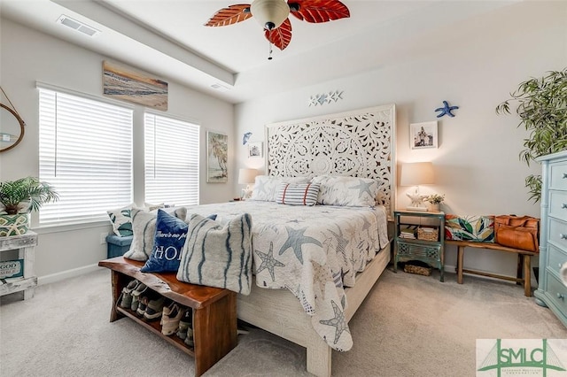 carpeted bedroom with a tray ceiling, a ceiling fan, visible vents, and baseboards