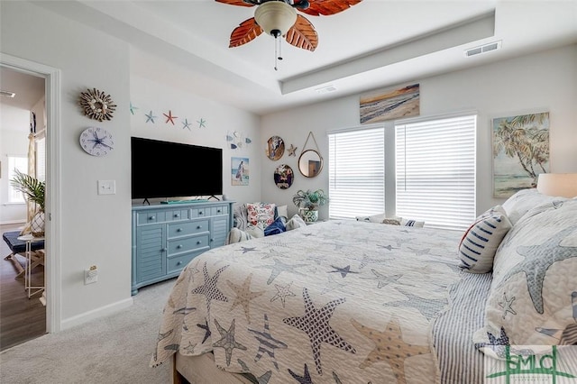 carpeted bedroom featuring baseboards, multiple windows, visible vents, and a tray ceiling