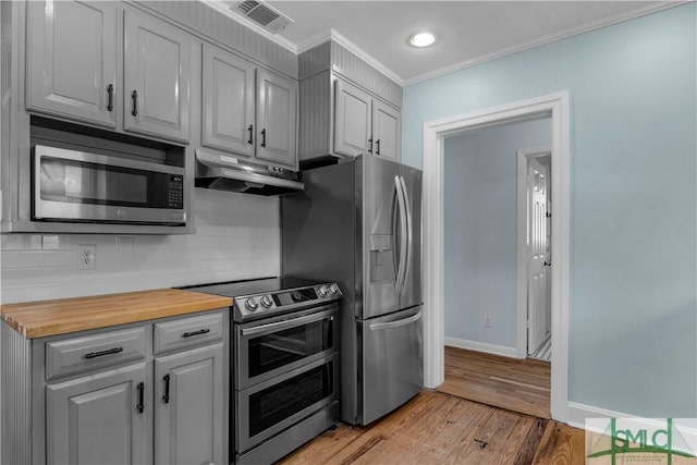kitchen featuring visible vents, crown molding, under cabinet range hood, stainless steel appliances, and butcher block countertops